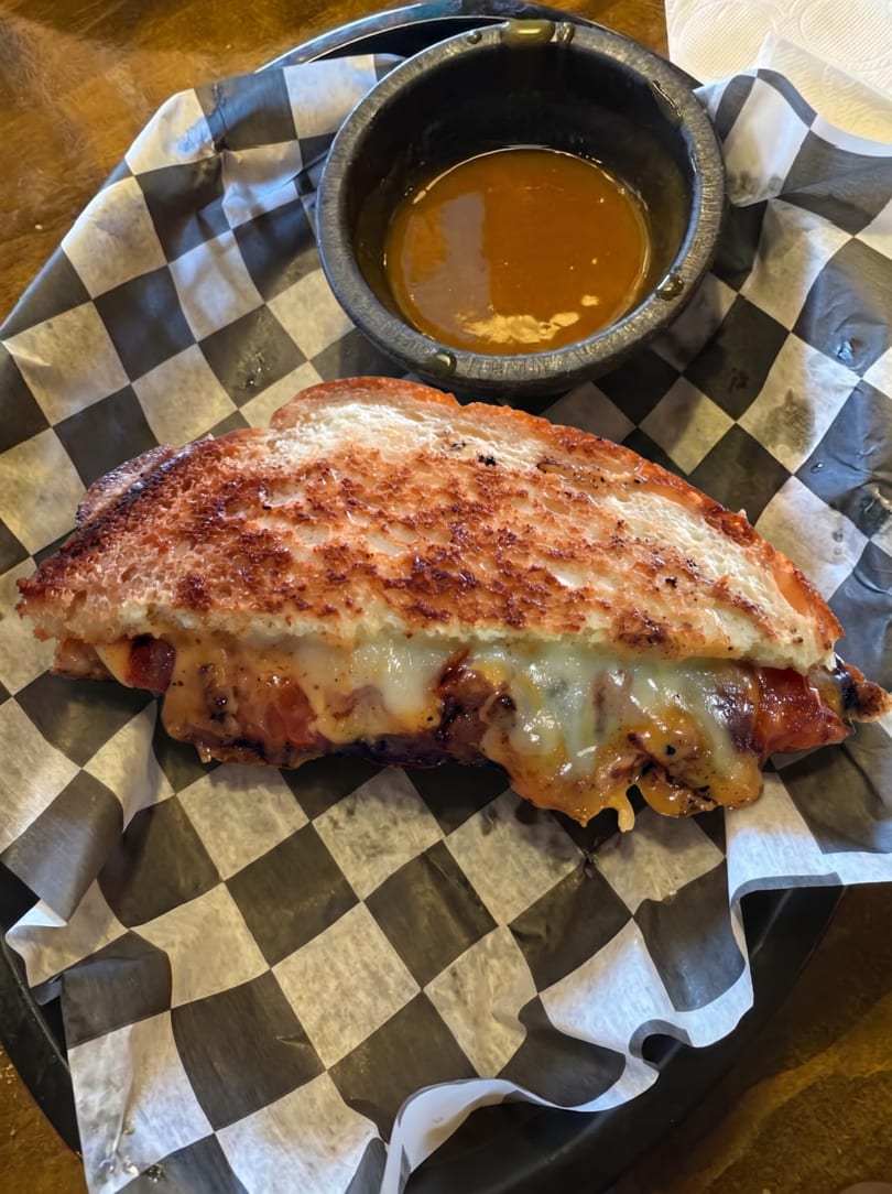Grilled cheese sandwich with melted cheese and red filling, served with a side of dipping sauce.